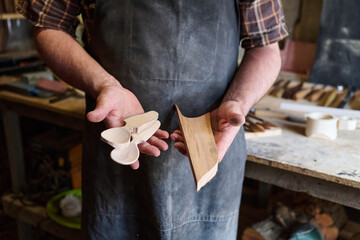 Craftsman holding wood carving pieces in workshop, showing handmade wooden spoons and block, woodworking process, artisan craft, traditional skill, handmade product photo