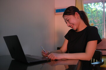A woman is sitting at a desk with a laptop and a pen