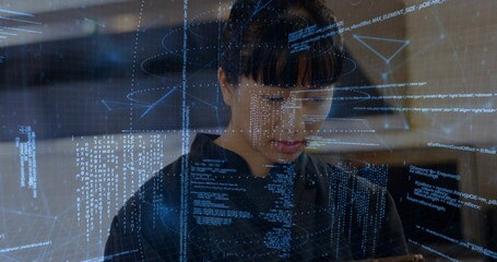 Mid adult Asian engineer analyzing code on holographic interface in tech lab, with handheld tablet