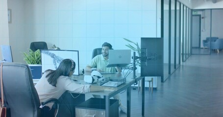 Collaborating colleagues in blouse and polo leaning over monitors at office with VR helmet