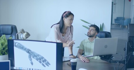 Obraz premium Pointing woman and seated coworker analyzing laptop and monitor rendering of robotic hand in office
