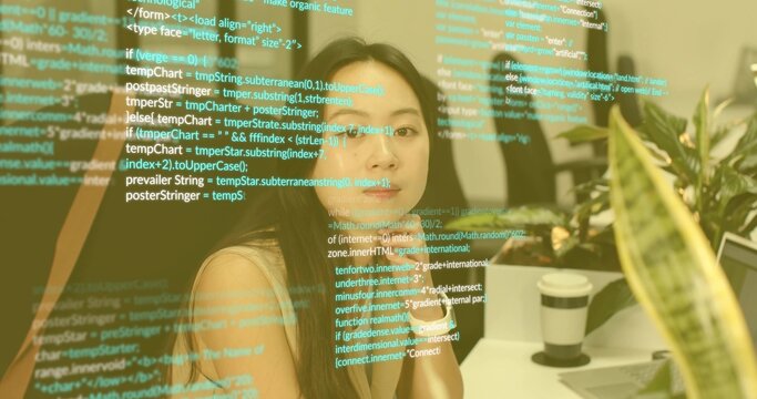 Analyzing transparent code display, Asian female sitting at office desk, with coffee cup and plant