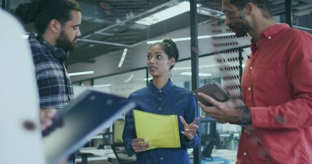Speaking woman wearing denim shirt holding yellow folder in office, colleagues using tablet