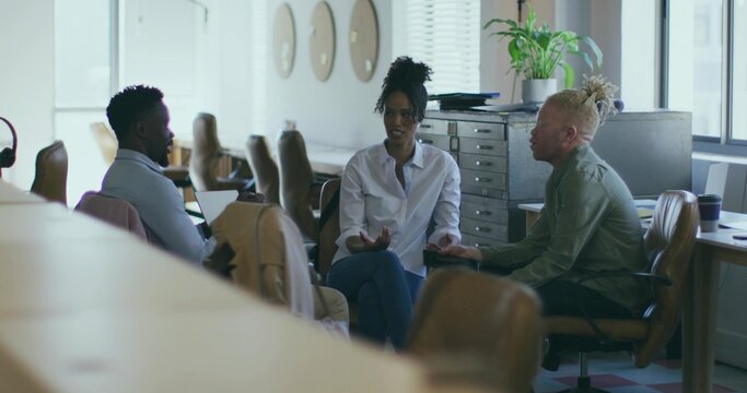 Discussing colleagues in shirts gesturing around laptop in open-plan office, with coffee cup - Powered by Adobe