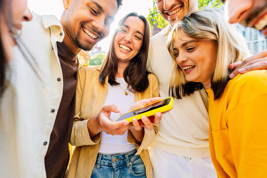 Happy group of diverse people having fun using mobile phone at city street. Social media and youth concept - Powered by Adobe