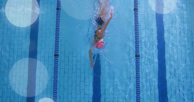 Gliding female swimmer stroking through tiled pool lane with cap goggles swimsuit and divider ropes
