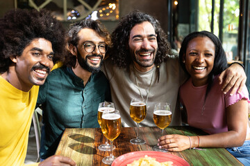 Multi-ethnic group of friends laughing and drinking beer at a bar, enjoying their time together