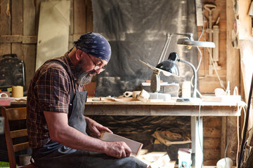 Craftsman sanding wood in workshop, woodworking project, artisan focused on handmade craft, skilled worker creating wooden object, carpentry in rustic environment, hobbyist at work