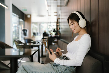 A young woman wearing white headphones smiles while using her smartphone outdoors, enjoying music or chatting in a bright, sunny environment.