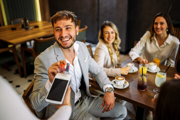 Friends enjoying drinks as man pays with card at restaurant
