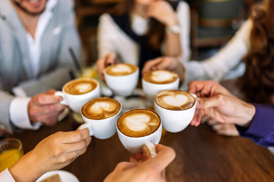 Group of friends cheering with coffee cups in cafe