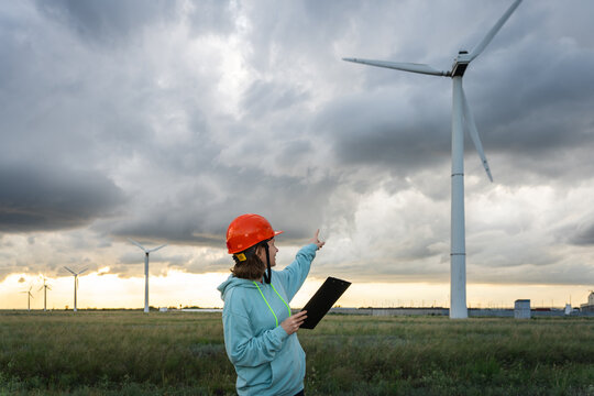 Woman in helmet assessing wind farm with clipboard