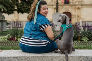Plus size woman sitting with her weimaraner dog in a park