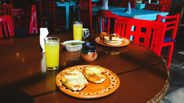 Mesa servida con desayuno completo: hotcakes, jugo, caf&eacute; y miel. Colores vivos y ambiente acogedor que invitan a disfrutar la comida.