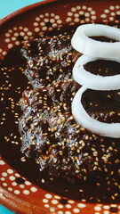 Platillo de enchiladas bañadas en mole, decoradas con rodajas de cebolla, lechuga y jitomate, servidas en plato de barro sobre una mesa turquesa.