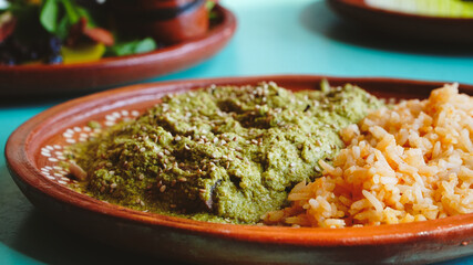 Platillo de pollo en salsa verde acompañado de arroz mexicano, servido en plato artesanal sobre mesa turquesa.
