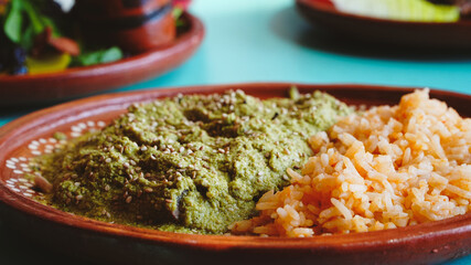 Platillo de pollo en salsa verde acompañado de arroz mexicano, servido en plato artesanal sobre mesa turquesa.
