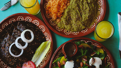 Mesa servida con enchiladas, ensalada fresca y pollo en salsa verde; bebidas tradicionales acompañan el conjunto.