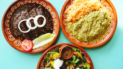 Vista aérea de mesa con tres platillos mexicanos coloridos: enchiladas de mole, pollo en salsa verde y ensalada fresca.