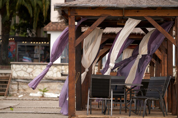 A beach gazebo with fabric curtains fluttering in the wind on the seashore.