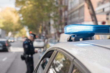 Police car with flashing lights parked on city street during patrol with officer in background © Jorge