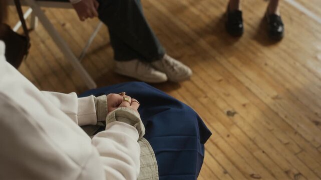 High angle of teenage girl wearing white sweatshirt and blue skirt sitting on chair between her schoolmates and explaining psychologist her problem during session