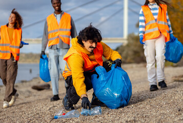Smiling volunteers collecting garbage in blue bags during river cleanup.