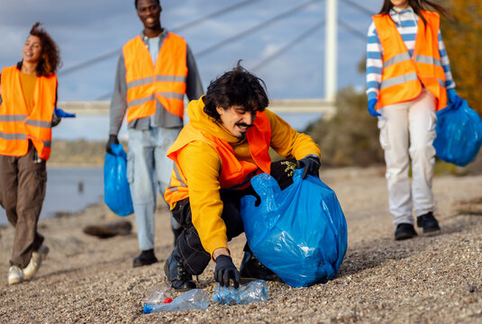 Smiling volunteers collecting garbage in blue bags during river cleanup. - Powered by Adobe