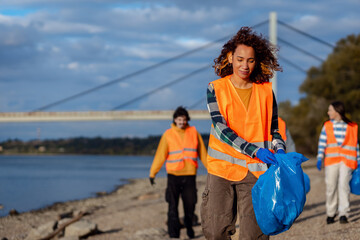 Smiling volunteers collecting garbage in blue bags during river cleanup.