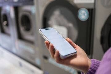 Young woman using smartphone while waiting for laundry in laundromat