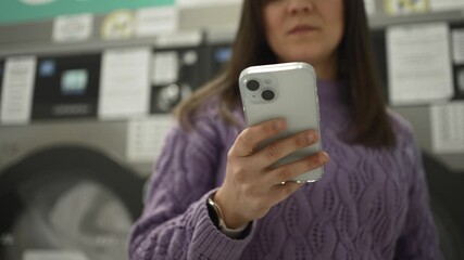 Young woman using smartphone in laundromat while waiting for laundry - Powered by Adobe