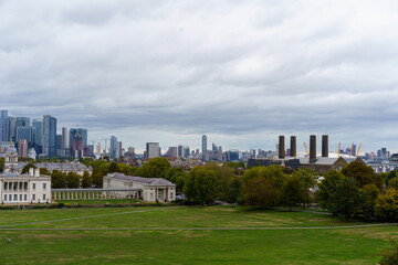 Obraz premium Overcast London panorama from Greenwich Park, blending historic architecture with the modern skyline of Canary Wharf and the O2 Arena, above green lawns.