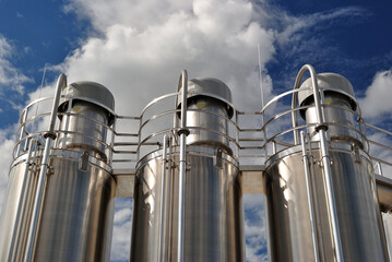 Three Shiny Stainless Steel Industrial Storage Tanks seen from Below against Blue Sky