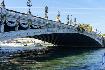 Obraz premium Ornate Pont Alexandre III bridge over the Seine River in Paris, with detailed sculptures, gold accents, and grand lampposts, under a clear blue sky.