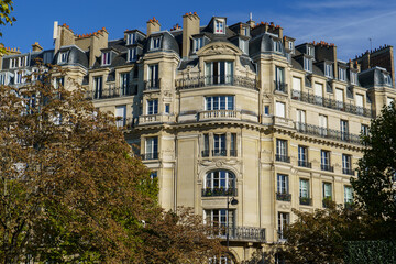 Haussmannian building in Paris with ornate details, balconies, and autumn trees under a clear blue sky.