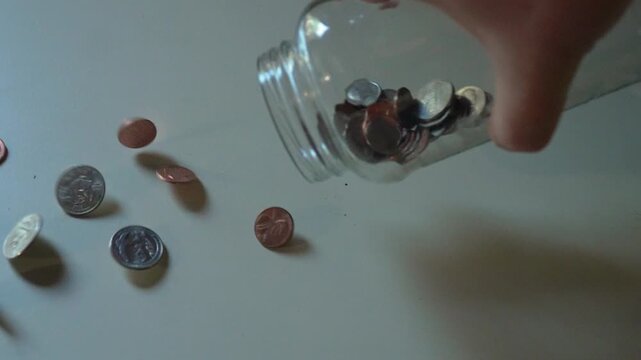 Man dumping coins out of a glass jar onto a countertop