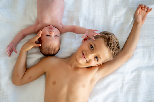 Siblings enjoying a moment together on white bed sheets