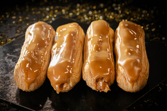 Four glazed coffee and caramel &eacute;clairs on a black background with golden bokeh