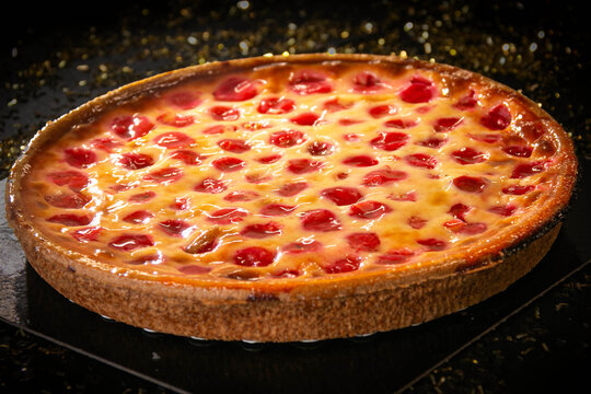 Traditional French cherry clafoutis tart with glistening red berries on a black background