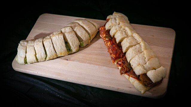 Stuffed appetizer bread with sun-dried tomatoes and green pesto on a wooden cutting board