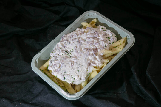 Italian penne carbonara in a takeaway plastic container on a dark background