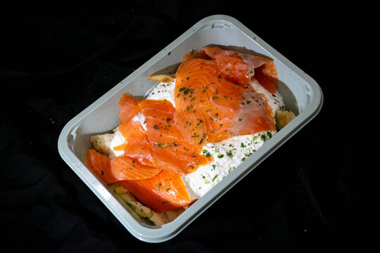 Smoked salmon pasta with creamy sauce in a takeaway container on black background