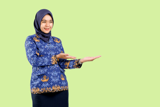 Smiling Indonesian teacher or government employee wearing blue ASN batik uniform presenting empty space with both hands, concept of education, communication, and professional promotion.