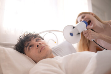 Playful woman using a megaphone to wake up her partner in the morning