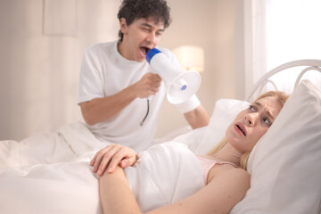 Obraz premium Playful man using a megaphone to wake up his partner in the morning