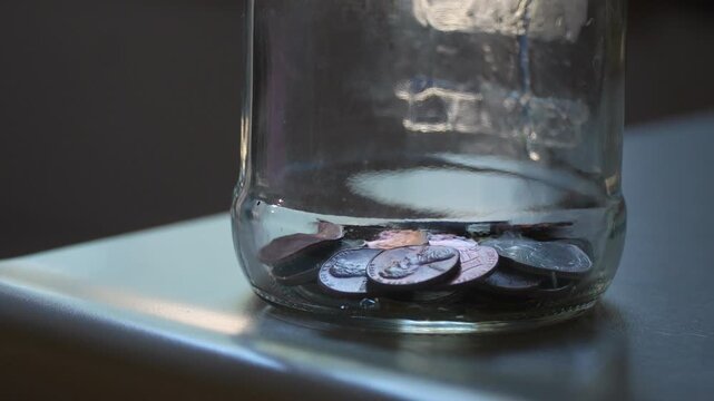 Close-up of coins falling into the bottom of a glass jar