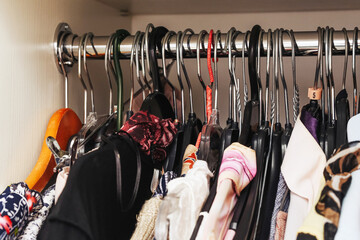 Clothes hanging on rack inside wardrobe. Colorful garments and hangers in bedroom closet. Fashion...