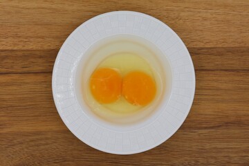 A raw chicken egg with two yolks on a plate isolated on a wooden background. Top view.