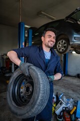 Mechanic holding a tire and smiling in a car repair shop