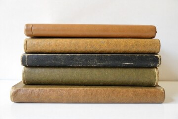 Stack of vintage books artfully arranged on a white backdrop, evoking a sense of history. A neat stack of 3 5 vintage hardcover books with textured, slightly worn bindings in muted colors, arranged